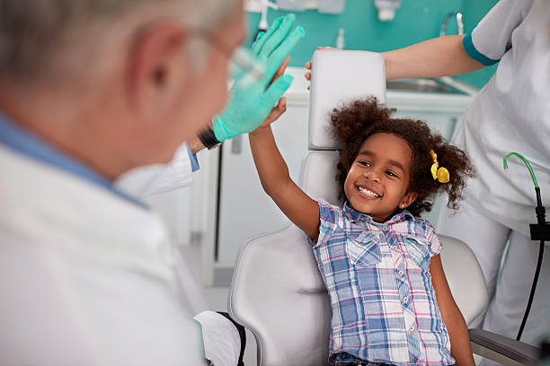 A child sitting in a dental chair gives a high-five to her dentist.