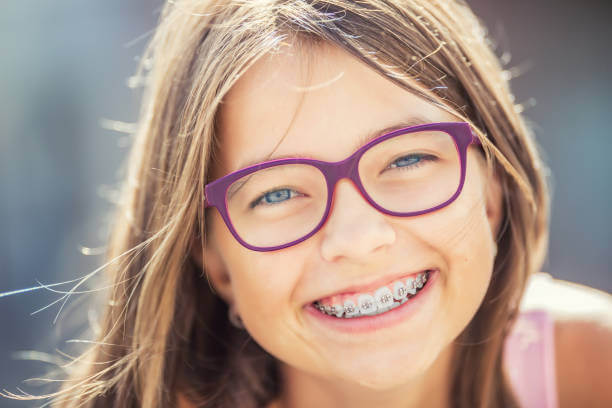 A girl wearing purple rimmed glasses smiles at the camera, showing off her metal braces.