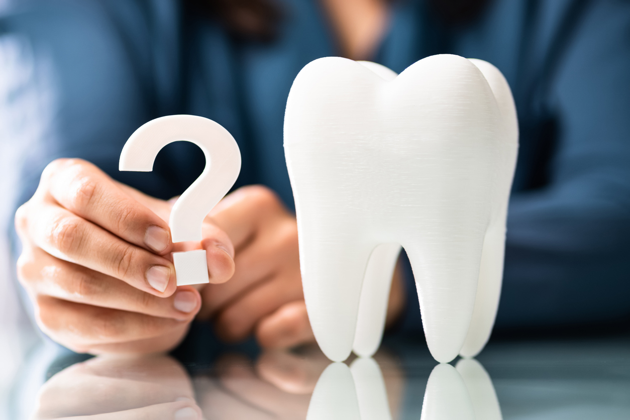 A dentist holds a question mark next to a large tooth. 