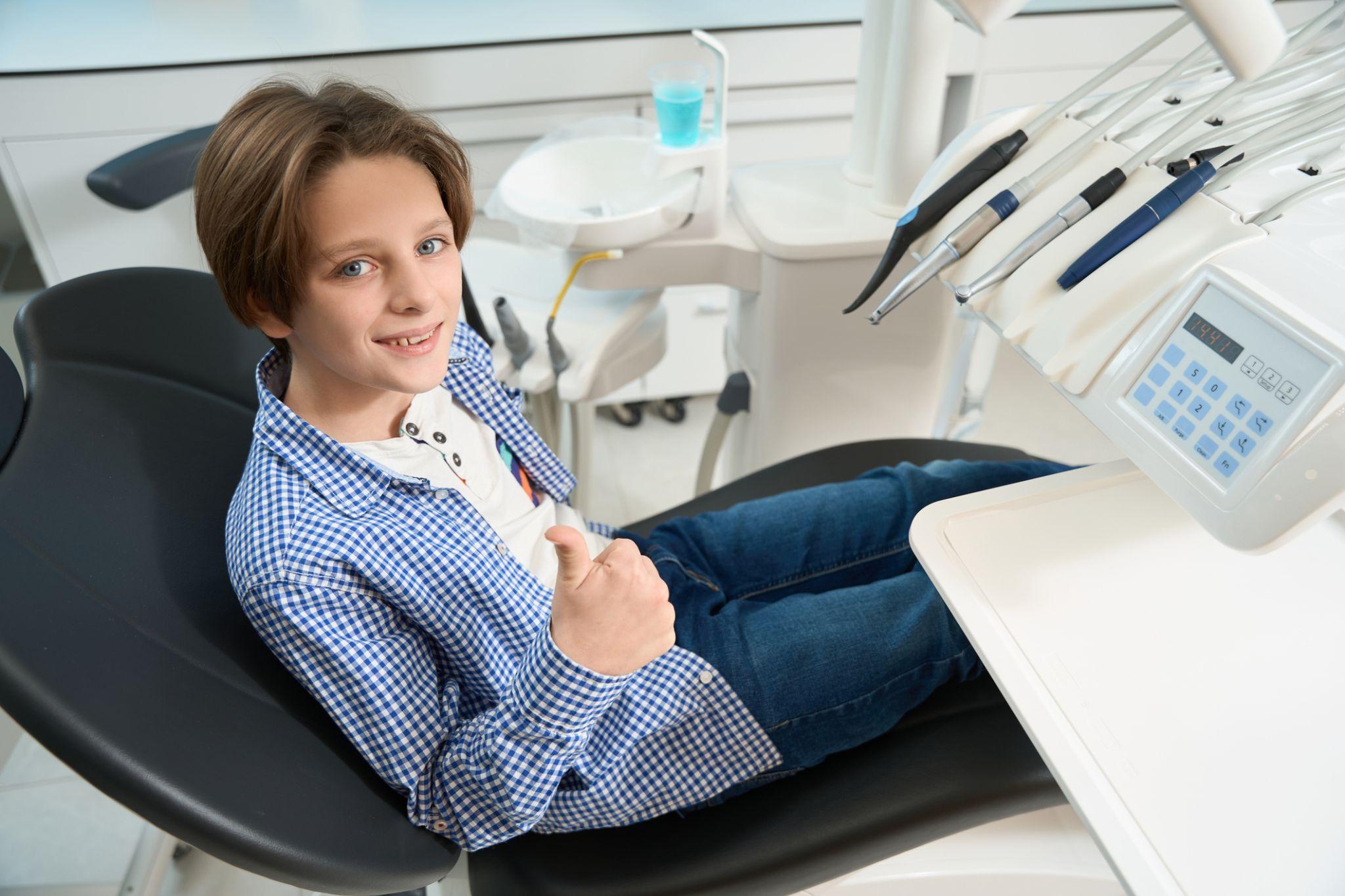 A child gives a thumbs up and smile while sitting in a dental chair.
