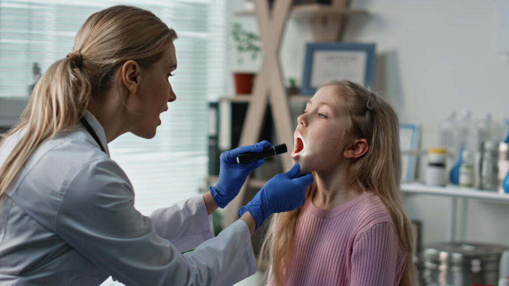 A dentist flashes a light into the mouth of a young girl.